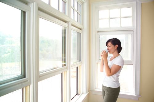 Woman drinking from a coffee mug while looking out of the window concept of window replacement in Madison